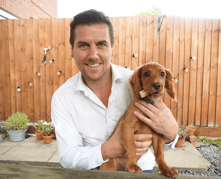 Photo of a man wearing a white shirt, holding a puppy in his arms